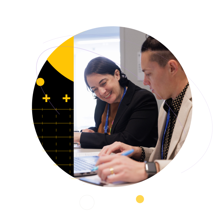 Two conference attendees working together on laptops, framed by yellow and black geometric patterns.