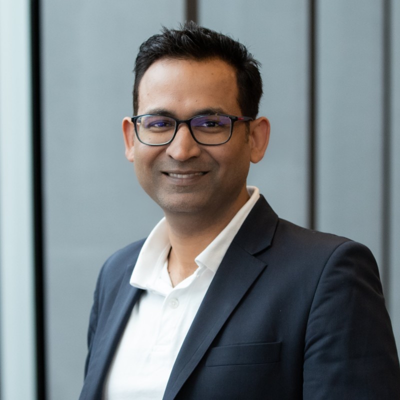 Headshot of Akash Mittal smiling, wearing glasses and a navy blazer.