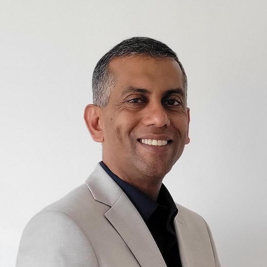Headshot of Jabez Abraham smiling, wearing a light gray blazer and black shirt.