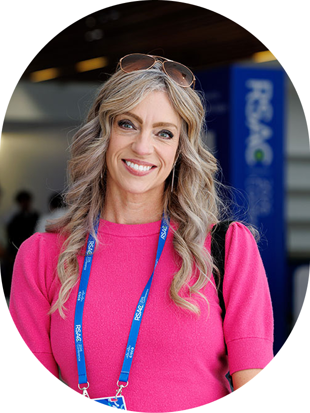 Smiling woman with long blonde hair wearing a bright pink top and RSAC conference lanyard.
