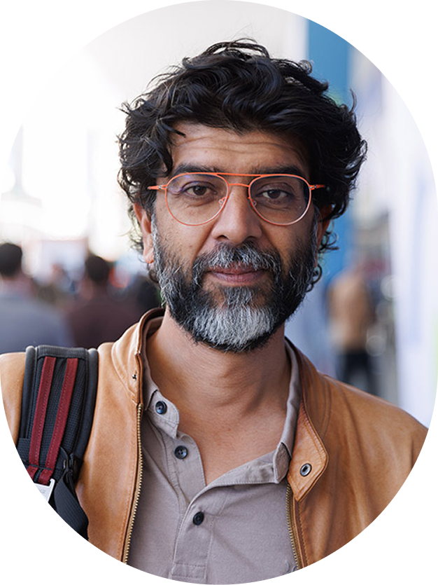 Man with curly dark hair, glasses, and a gray beard wearing a tan jacket.