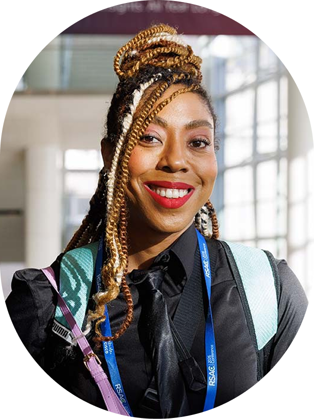 Smiling woman with blonde braids wearing a black shirt and RSAC conference lanyard.