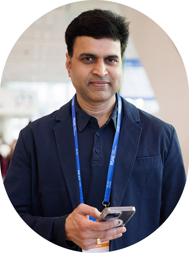 Man with short dark hair wearing a navy blazer and holding a smartphone at a conference.