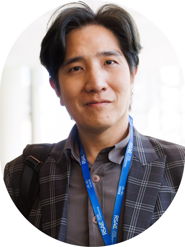 Man with dark hair wearing a plaid blazer and blue RSAC conference lanyard.