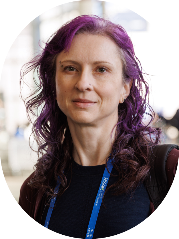 Woman with wavy purple hair wearing a black top and RSAC conference lanyard.