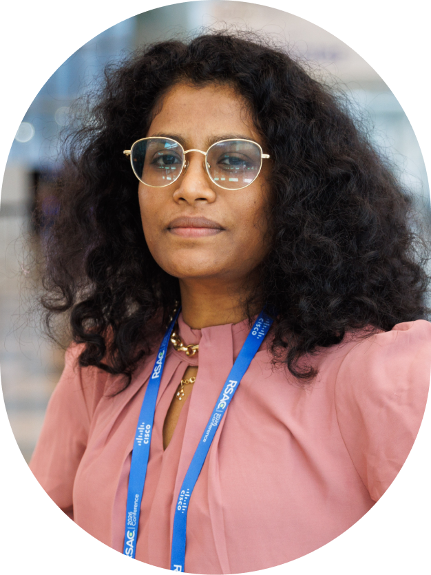 Woman with curly dark hair and glasses wearing a pink blouse and RSAC conference lanyard.