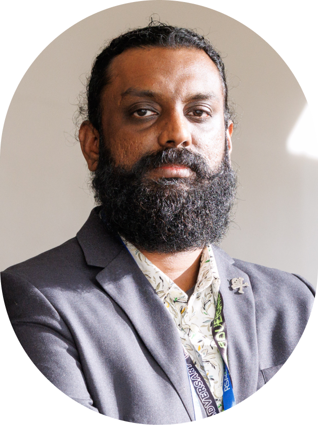 Man with a full beard wearing a gray blazer and conference lanyard.