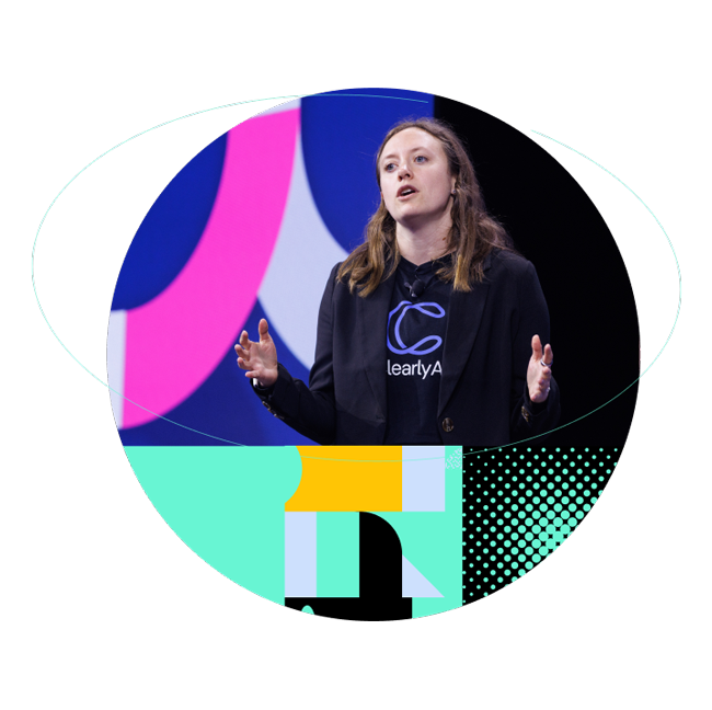 Woman presenting on stage at a technology conference, surrounded by vibrant pink, teal, and blue geometric shapes.