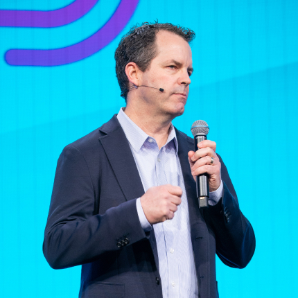 Male speaker holding a microphone on stage, representing Soluble, a 2020 RSAC Launch Pad finalist acquired by Lacework.