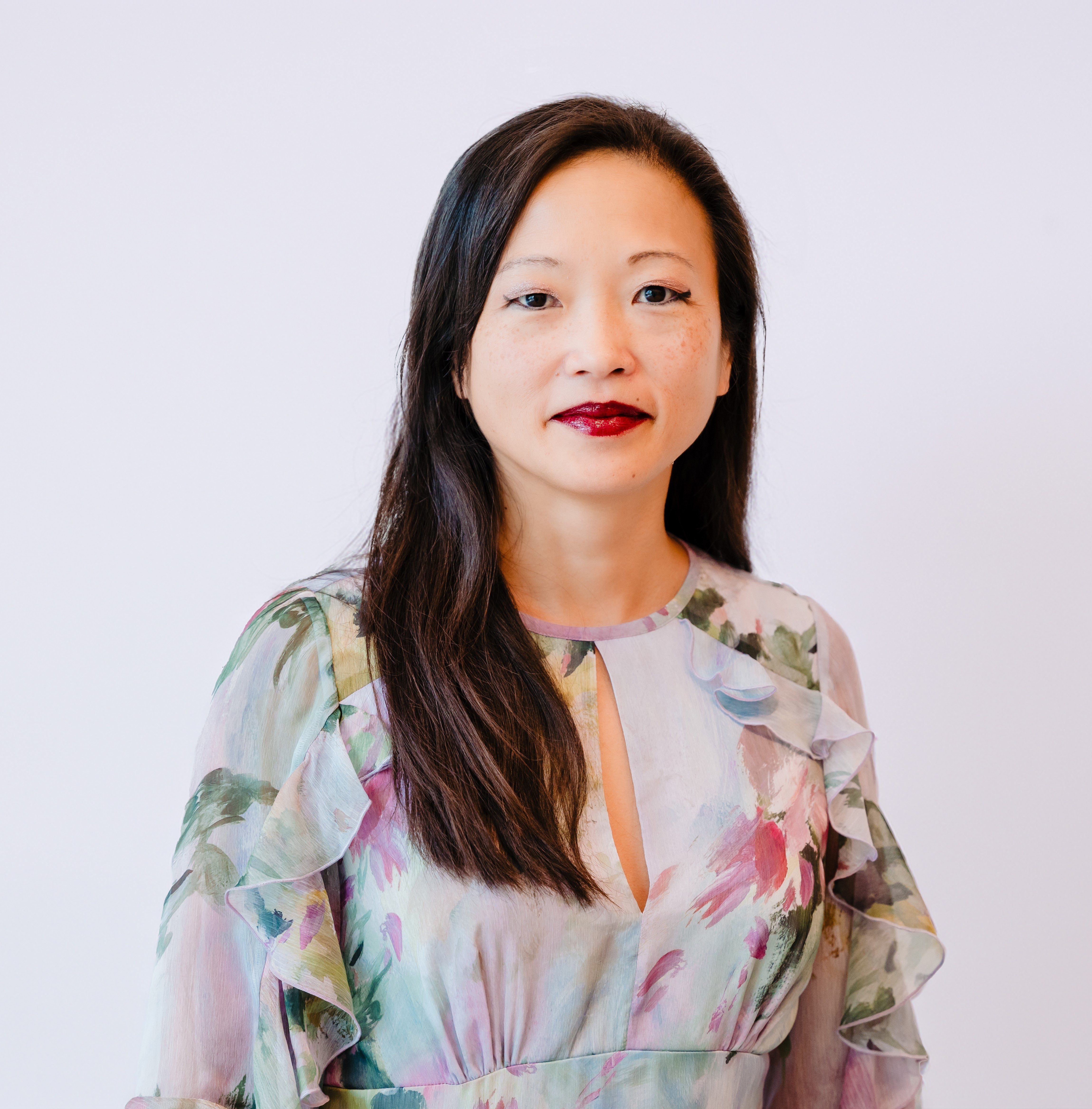 Professional portrait of a woman with long dark hair wearing a floral-patterned blouse.