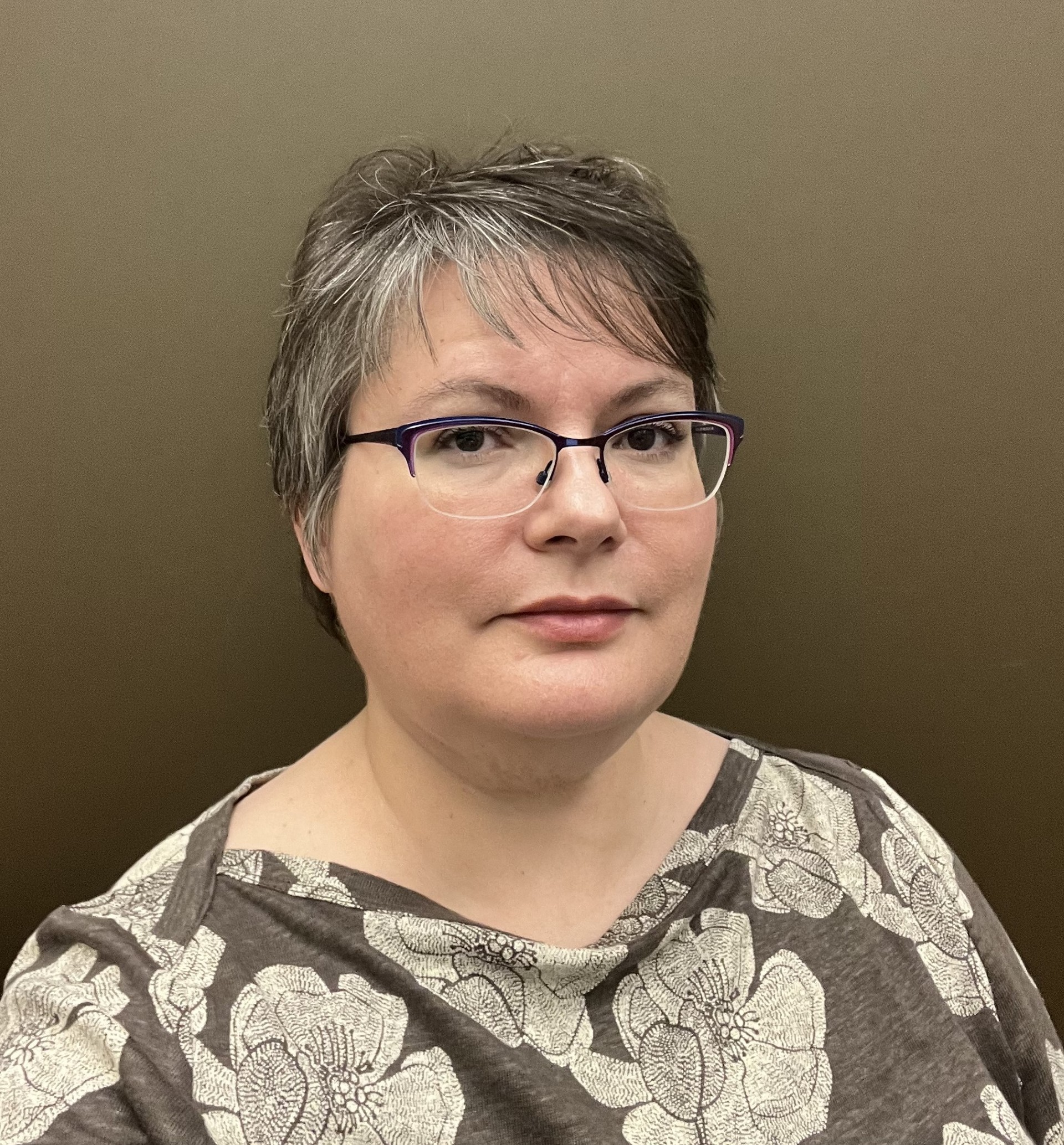 Professional headshot of a woman with short gray hair and glasses wearing a patterned top.