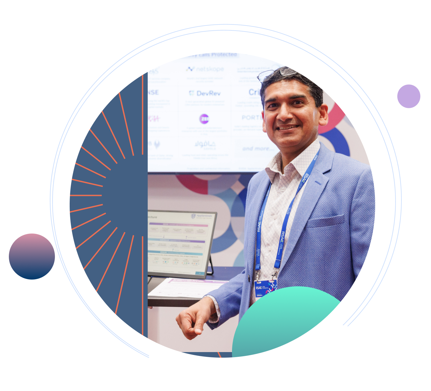 Smiling man wearing a light blue blazer and RSAC conference badge standing at an exhibition booth, framed by blue and orange geometric patterns.