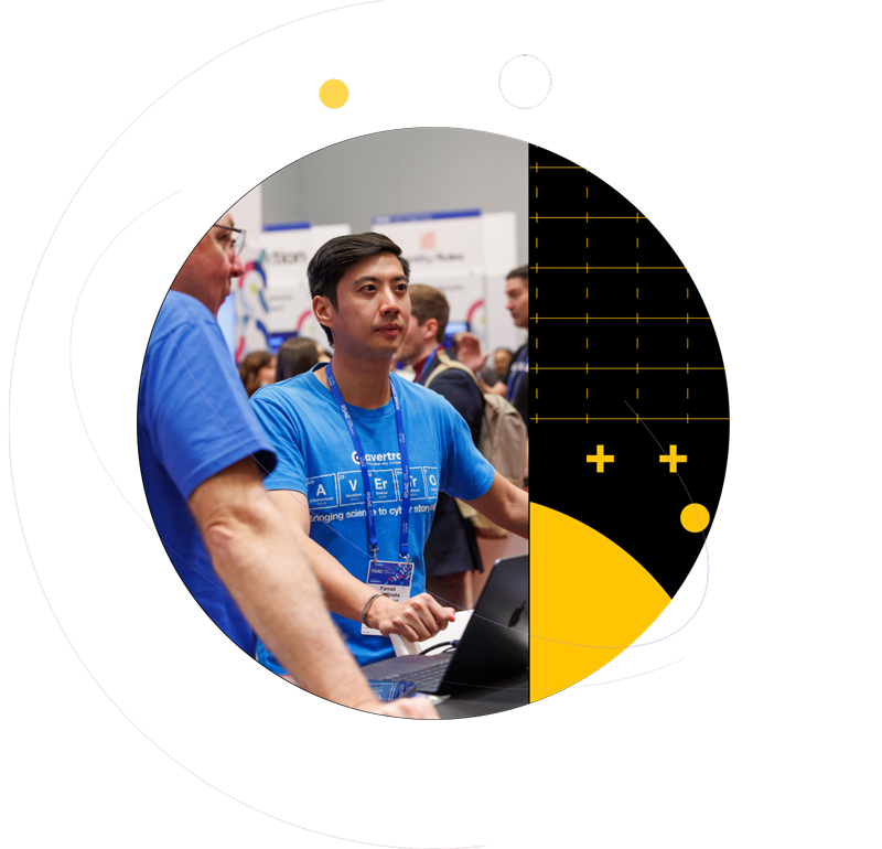 Two men discussing a technology demonstration at an RSAC exhibition booth, framed by black and yellow geometric patterns.