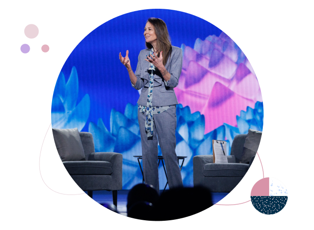 Woman speaking on stage at an RSAC event, gesturing with both hands in front of a colorful blue and purple backdrop.