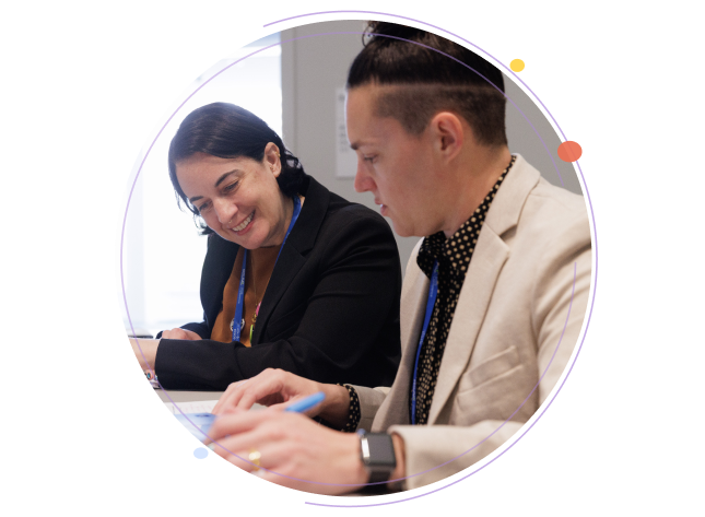 Two conference attendees smiling and collaborating while reviewing documents at a table, framed by circular graphics.